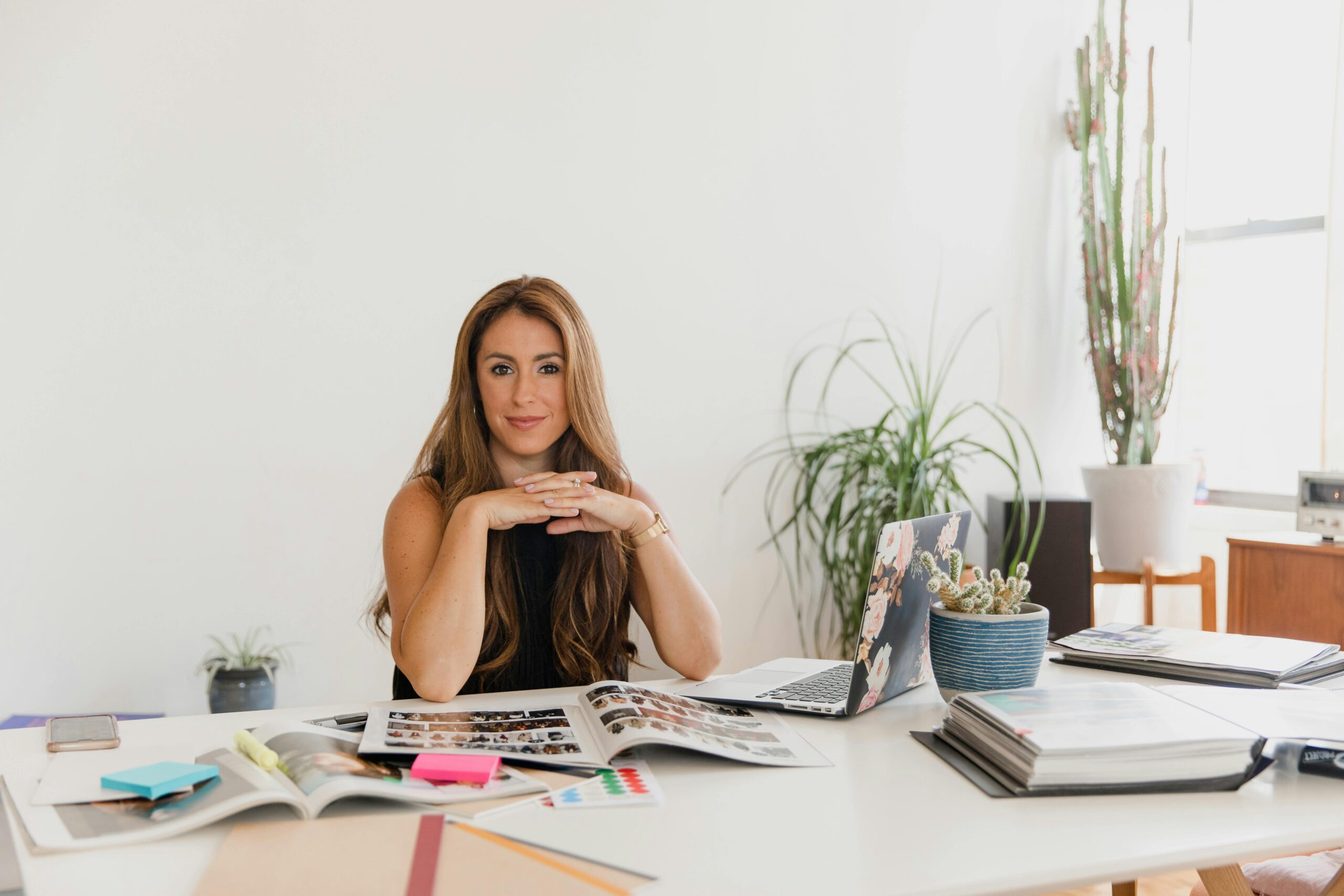 business-frau-im-office Geschäftsfrau Mitte 40 sitzt entspannt mit verschränkten Fingern an einem hellen Schreibtisch‐Setup mit Grünpflanzen